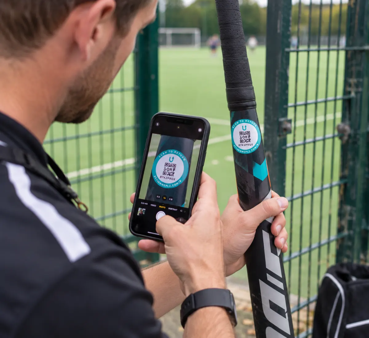 A coach scanning the ReturnMePlz label on a hockey stick beside the school pitch